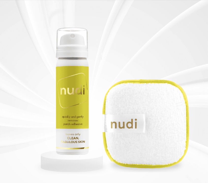 50ml Nudi Spray standing on a white podium next to a cleansing Nudi Pad